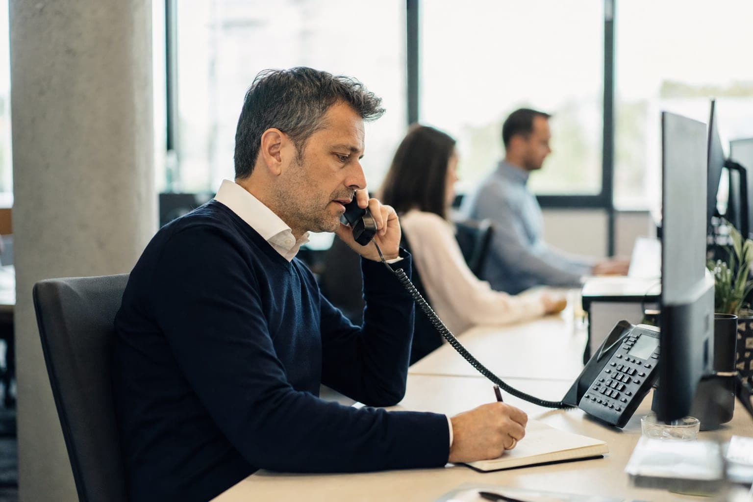 Recruiter im Büro am Telefon, daneben Notizblock und Tischapparat